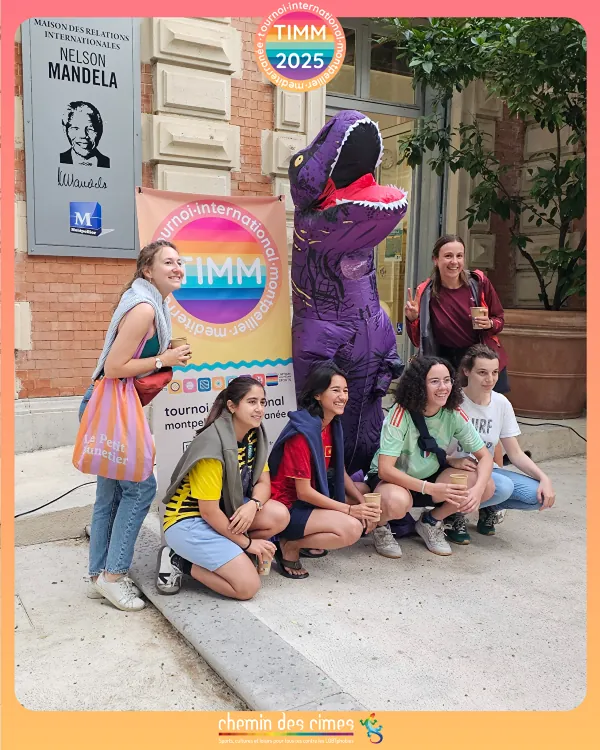 Un groupe pose avec Timmo, la mascotte dinosaure du tournoi, devant la Maison des relations internationales Nelson Mandela.